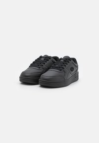Svarta sneakers i slät läder med snörning, rund tå, texturerad gummisula och minimal branding på sidan.