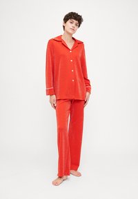 Red, sparkly pajama set featuring a collared button-up top and matching pants with a relaxed fit and white accents on the cuffs.