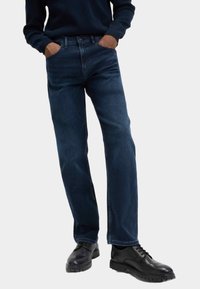 Mörka denimjeans med rak passform, med framfickor, i kombination med svarta läderskor och en marinblå tröja.