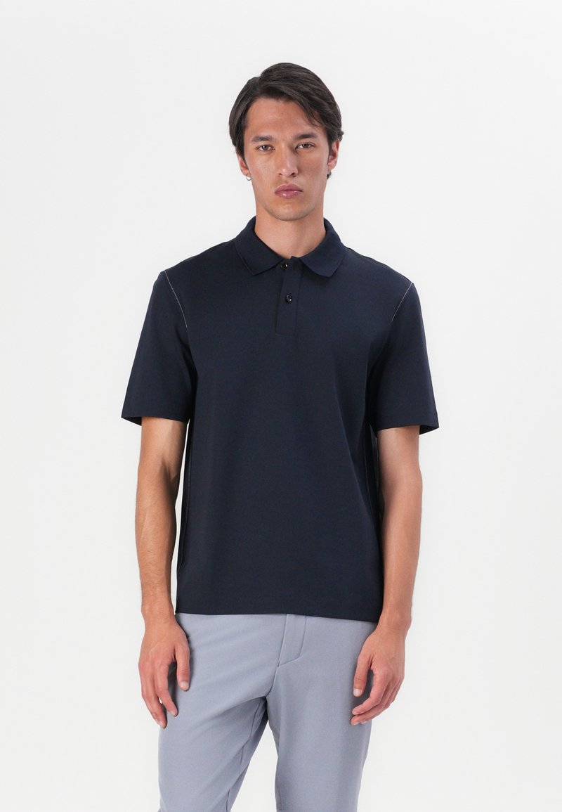 Tumesinine polosärk lühikeste varrukatega, krae, kolme nupuga klapp ja peened õmblusdetailid. Kanna koos heleda halli pükstega.