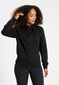 Felpa nera con zip e colletto alto, cordini regolabili, polsini a coste e una piccola etichetta con logo sull'orlo. Tessuto morbido in misto cotone.