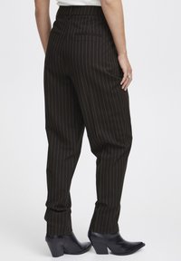 Zwart gestreepte broek met een hoge taille en toelopende benen. Heeft achterzakken en wordt gecombineerd met spitse zwarte enkellaarsjes.