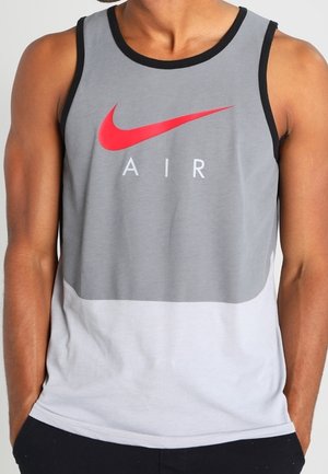 Szara i biała koszulka bez rękawów Nike z czarnymi akcentami. Z przodu znajduje się czerwone logo Swoosh oraz napis "AIR". Wykonana z lekkiego materiału.