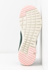 Idrottssko med en texturerad vit gummisula och rosa detaljer. Mörkgrön överdel i textil har en strömlinjeformad design.