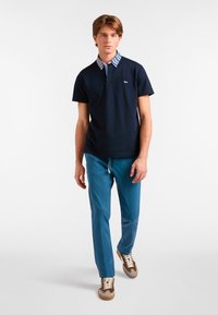 Granatowa koszulka polo z paskowanym kołnierzykiem, w zestawie z niebieskimi spodniami. Model nosi wielokolorowe sneakersy. Gładki materiał, swobodny krój.