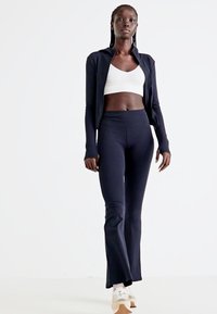Marineblaue Sportbekleidung bestehend aus einem eng anliegenden Oberteil und weit geschnittenen Hosen. Glatte Textur, dehnbarem Material und langen Ärmeln an der Jacke.