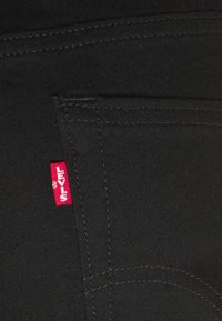 La tela de mezclilla negra presenta una etiqueta roja de Levi's. Las costuras son de un color contrastante, destacando los detalles de diseño y la estructura de los bolsillos.