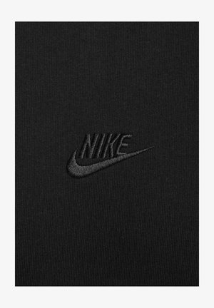 Juodas Nike marškinėliai, turintys tekstūruotą, siuvinėtą logotipą šiek tiek tamsesnio juodos atspalvio ant lygios, megztos medžiagos fono.