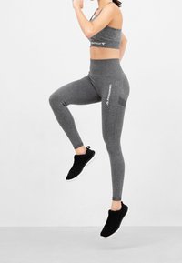 Szare legginsy sportowe i dopasowany krótki top, z gładką teksturą i detalem logo, w połączeniu z czarnymi sneakersami.