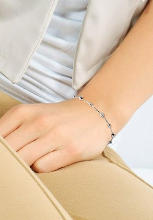 Bracelet en chaîne argentée avec des perles rondes de tailles variées. Texture lisse, design minimaliste, porté au poignet sur un fond clair.