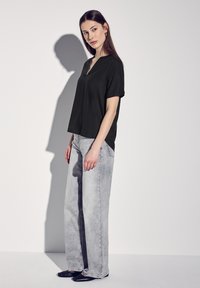 Top nero a maniche corte con scollo a V, abbinato a jeans a gamba larga grigio chiaro. Tessuto morbido, vestibilità rilassata, design minimalista, ombra sottile.