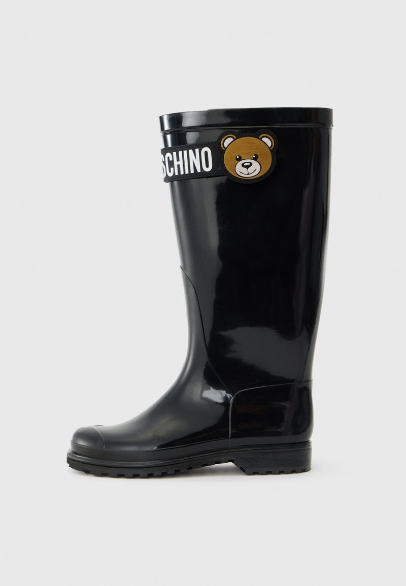 Botte de pluie en caoutchouc noir avec une finition brillante, bout rond, semelle texturée et un emblème d'ours avec le texte "Moschino" sur le côté.