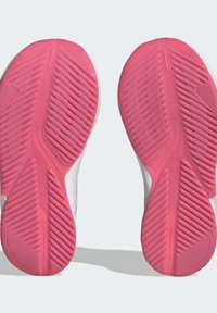 Scarpe sportive con una tomaia bianca e una suola in gomma rosa strutturata, caratterizzata da scanalature diagonali per trazione e aderenza.