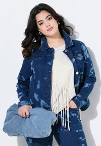 Denimjakke med et tie-dye mønster i blå og hvid, med knaplukning og brystlommer, parret med en cremet top med frynser.
