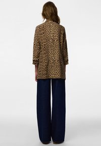 Casaco com estampa de leopardo e mangas compridas, fabricado em tecido macio, combinado com calças de ganga escuras de pernas largas. Vista traseira exibida.