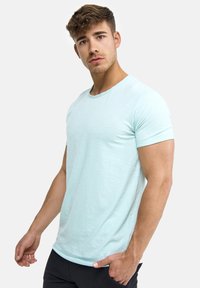 Light aqua short-sleeve t-shirt with a round neckline, smooth texture, and subtle stitching detail. Worn with black pants.