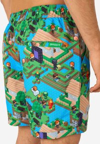 Farebné plavecké šortky s plánom na tému Minecraft, s modrým pozadím, rôznymi blokovými postavami a detailom zadnej vrecka.