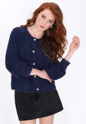 Navy blue, fuzzy knit cardigan with a round neckline, long sleeves, and gold buttons down the front. Styled with a black denim skirt.