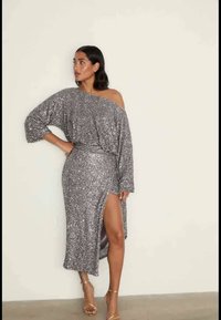 Hopeinen paljettimekko olkapäät paljastavalla mallilla, pitkät hihat, vartalonmyötäinen siluetti ja reisiin ulottuva halkio, yhdistetty remmikorkoihin.