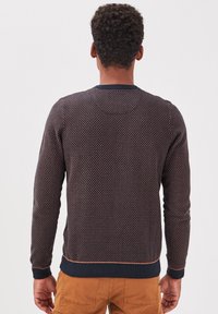 Jersey de punto azul marino con patrón geométrico texturizado, que presenta un cuello redondo y puños y dobladillo acanalados. Los detalles incluyen costuras en contraste.