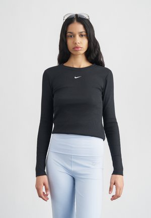 Črna dolga majica z rebrastim vzorcem in belim logotipom Nike nad prsmi, združena s svetlo modrimi visokimi legicami.