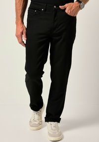 Pantalones de mezclilla negra con corte recto, que incluyen bolsillos frontales, cierre de botón y puños enrollados, combinados con zapatillas blancas.