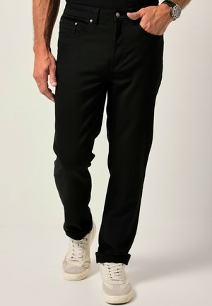 Zwarte denim broek met een rechte pasvorm, voorzien van voorzakken, een knoopsluiting en opgerolde manchetten, gecombineerd met witte sneakers.
