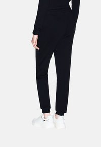 Pantaloni jogger neri con vestibilità affusolata, vita elastica e polsini a costine; abbinati a sneakers bianche e massicce con dettagli a catena.