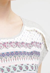 Lichtgewicht t-shirt met een grijs bovenste gedeelte en een gemusterd onderste deel met florale en geometrische ontwerpen in roos, blauw en wit.