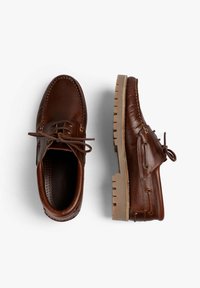 Zapatos náuticos de cuero marrón con empeine texturizado, cierre de cordones y suela de goma de color claro y contraste, con ranuras para mayor tracción.