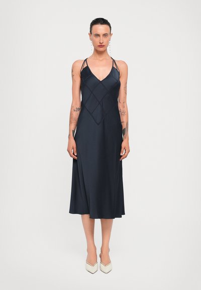 Navy satin dress with a V-neck, thin straps, and diamond pattern detailing. Flared hem extends to mid-calf; paired with beige pointed toe heels.