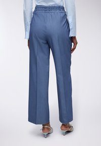 Pantaloni azzurri chiari a vita alta con una vestibilità morbida, realizzati in un tessuto testurizzato e dotati di un cintura strutturata. Fessure all'orlo aggiungono un tocco di dettaglio.