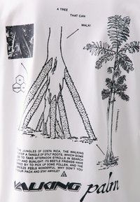 White t-shirt featuring black illustrations of a walking palm tree, with roots, leaves, and text describing the tree's characteristics.
