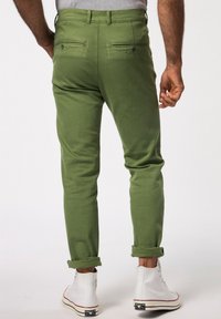 Pantaloni in cotone verde con vestibilità slim, con risvolti, due tasche posteriori e una trama liscia, abbinati a sneaker alte bianche.