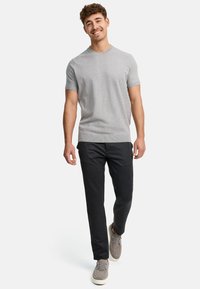 Lichtgrijze gebreide korte mouwen trui, gecombineerd met donkergrijze slim-fit broek en grijze casual schoenen. Man loopt naar voren.