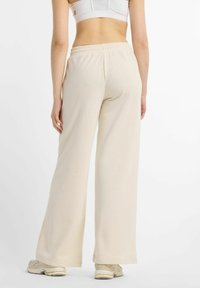 Pantalon large beige clair avec une ceinture élastique confortable et une texture douce, porté avec des baskets claires.