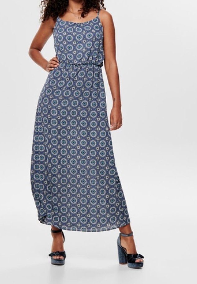 Femme portant une robe longue sans manches bleu à motifs avec des talons compensés à bride à la cheville, debout avec une main sur la hanche.