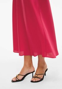 Fuchsia maxi-kjole med en flytende silhuett, kombinert med svarte hæler med stropper, dekorert med gullaksenter og tynn stiletthæl.