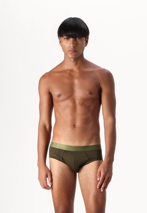 Braune Boxer-Shorts mit einem kontrastierenden grünen Bündchen, die eine glatte Textur und einen körperbetonten Schnitt aufweisen, präsentiert von einer oberkörperfreien Person.