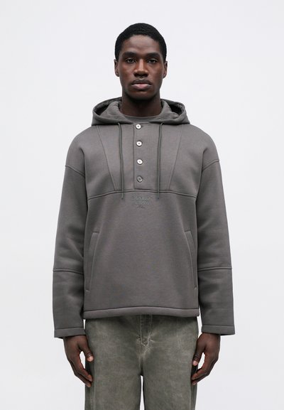Hanorac gri cu glugă, cu un finisaj texturat, având o închidere cu nasturi, buzunare laterale și logo brodat pe piept.