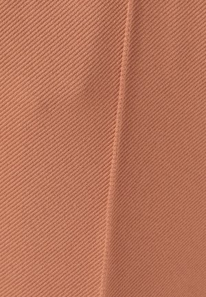 Tissu texturé dans une teinte corail douce et atténuée, présentant des crêtes diagonales et un détail de couture, suggérant un design structuré et un matériau léger.