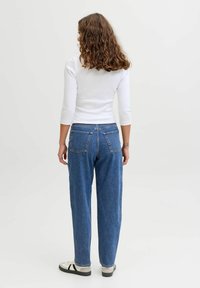 Zilas džinsa bikses ar vaļēju piegriezumu, tām ir aizmugurējās kabatas un augsts viduklis, valkātas kopā ar pieguļošu baltu topu un ikdienišķiem sporta apaviem.