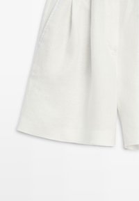 Pantaloncini bianchi plissettati con tasche laterali, realizzati con un tessuto leggero.