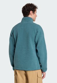 Polarowa kurtka w odcieniu teal z miękkim, teksturowanym wykończeniem. Posiada stojący kołnierz, długie rękawy i luźny krój. Casualowy design.