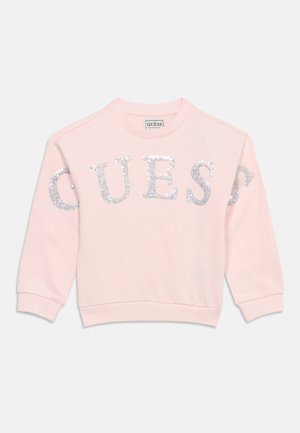 Lys rosa langermet genser med sølvglitrende bokstaver som staver "GUESS" over brystet, med ribbestrikkede mansjetter og kant.