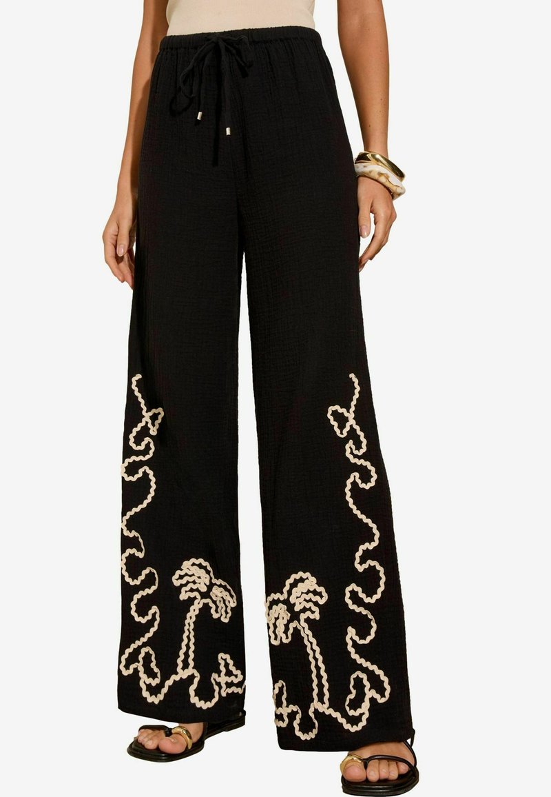 Wide-leg black pants in textured fabric, featuring contrasting cream palm tree and wavy line embroidery along the hems. Drawstring waist.