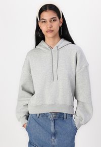 Sudadera gris corta con capucha ajustable, mangas anchas y dobladillo acanalado, combinada con pantalones cortos de mezclilla de talle alto.