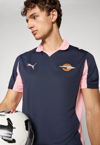 Tamsiai mėlyna ir rožinė trumpomis rankovėmis polo marškinėliai su apykakle, Puma logotipu ir Palermo FC emblema. Matoma tekstūruota medžiaga ir sportiškas kirpimas.