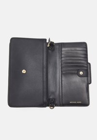 Portafoglio in pelle nera con una texture liscia; presenta vari slot per carte, una tasca con zip e dettagli in metallo dorato. Marchio "MICHAEL KORS" visibile.