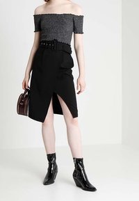 Czarny top bez ramiączek z teksturowanym wzorem, zestawiony z czarną spódnicą o wysokim stanie z paskiem i rozcięciem z przodu. Czarne botki na obcasie.